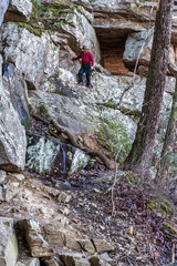 A man on a mountain hiking on a steep rocky bluff trail to a rock tunnel in winter. Beautiful hike on the Perimeter Trail in Sewanee, Tennessee USA.