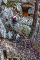 A man on a mountain hiking on a steep rocky bluff trail to a rock tunnel in winter. Beautiful hike on the Perimeter Trail in Sewanee, Tennessee USA.