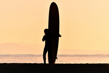 早朝の砂浜に立つサーファー（シルエット）