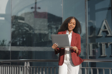 Beautiful african american business woman in red formal suit leader entrepreneur, professional manager holding digital tablet, going to work, walking urban outdoor, standing on city street