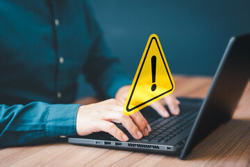 Adult man using computer laptop with triangle caution warning sign for notification error. Computer virus detected, personal data protection, network security and maintenance concept. - 559959947