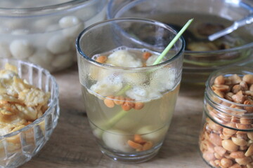 A traditional Indonesian drink called wedang ronde containing ronde, peanuts, and emping melinjo in a glass cup on a wooden table