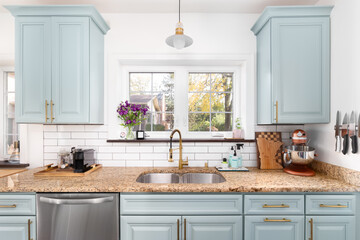 A light blue kitchen detail with a granite countertop, gold faucet and light, and a white subway tile backsplash.