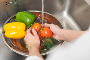 Close up asian young woman washing tomato, broccoli, carrot fresh vegetables, paprika with splash...