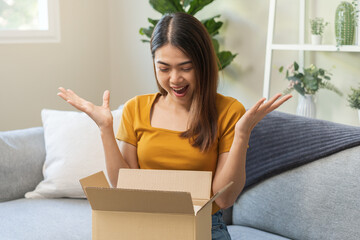 Happy excited, asian young woman, girl customer sitting on sofa at home, open and unpack cardboard box carton parcel after buy fashion clothes, ordering present and shopping online, delivery service.