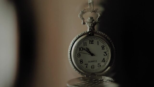 Silver pocket watch moving in slow motion used to induce a state of hypnosis, close up shot