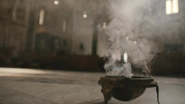 Footage of a bowl of incense on the floor of a church smoking in Bari, Italy.