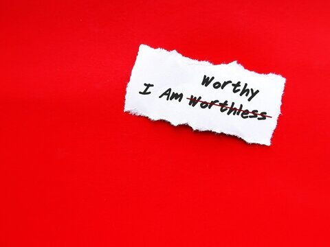 Torn white paper on red copy space background with handwritten text I AM WORTHLESS change to I AM WORTHY, concept of self talk affirmation to build self esteem and acceptance