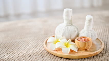 Fototapeta na wymiar Spa herbal balls, Himalayan salt and frangipani flowers on a wooden tray on massage table.
