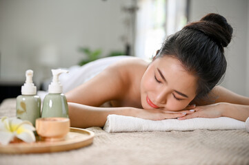 Relaxed Asian woman lying on massage table with eyes closed, waiting for Thai massage