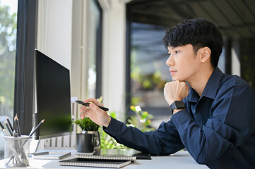 Smart Asian male office worker or businessman focusing on his task, looking at computer screen