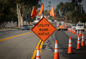 Traffic sign with flags reading Utilitary Work Ahead with traffic cones on road with electronic...