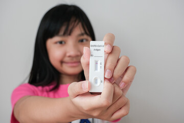Asian girl holding red line Antigen Rapid Test (ATK) test kit 1, negative during COVID-19 swab test.