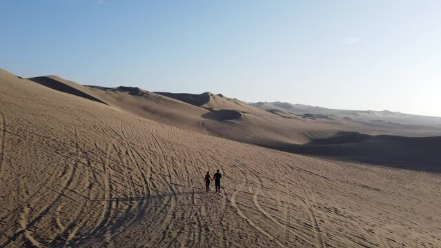 The travelers walk through the desert to meet the buggy car. Huacachina, Peru