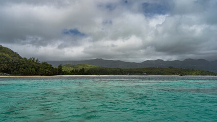 Ripples on the surface of the turquoise ocean. In the distance you can see a tropical island overgrown with green vegetation, a sandy beach. Clouds in the blue sky. Seychelles