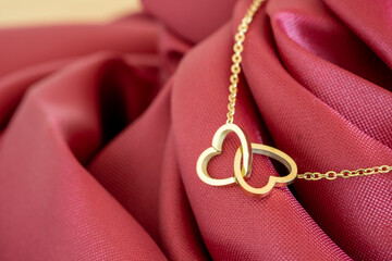 A gold necklace with a gold heart-shaped pendant resting on a pinkish-red fabric is the perfect gift for love, anniversary or special occasions on Valentine's Day. - obrazy, fototapety, plakaty