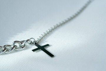 silver or stainless steel necklace with a cross pendant rests on a white cloth.