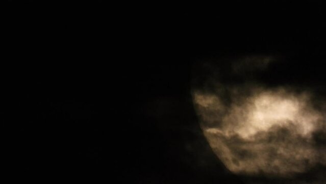 Illuminated close-up of the moon in the dark sky with clouds passing by