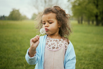 Nature, relax and child with blowing a dandelion for a wish, playing and exploring on a field in Norway. Spring, playful and girl with a flower plant in a park for calm, peace and outdoor adventure
