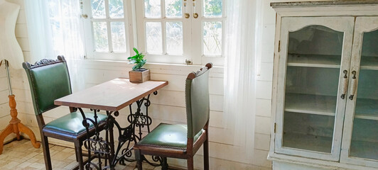 Sunny living room in warm colors with cozy chair, vintage cupboard, plants and large windows, nostalgic