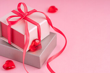 Two carton gift boxes of silver and beige colour with bow made of textile red ribbon laying on pink background with copy space and heart shaped decorations prepared for celebration of velentines day