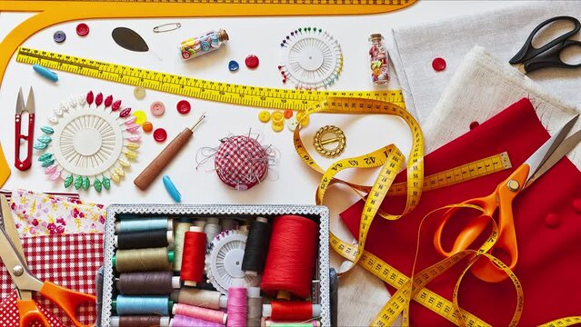 Close-up view on accessories for cutting and sewing: different types of scissors, chest with set of threads, curve and rulers for cutting fabrics, buttons and needles on white table. Home sew concept