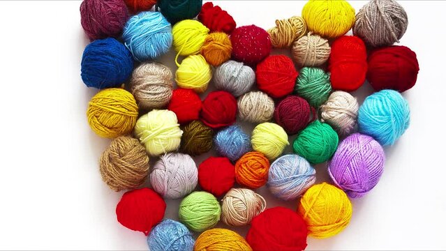 Set of colorful balls of woolen yarn for hand knitting and crocheting in shape of heart on white background. Handmade and DIY concept. Flat lay, mock up, top view, closeup. Turning movement