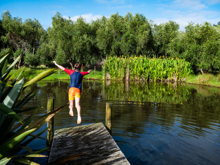 Fototapeta na wymiar A boy is jumping into a natural pond during summer