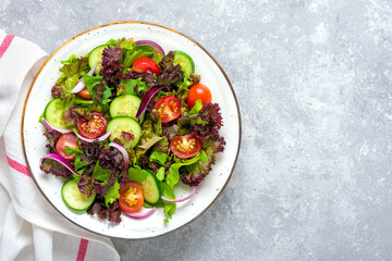 Healthy vegetable salad of cherry tomatoes, cucumber slices, green and purple lettuce leaves, onions and olive oil in plate on concrete table Top view Flat lay Diet, mediterranean menu Vegan food