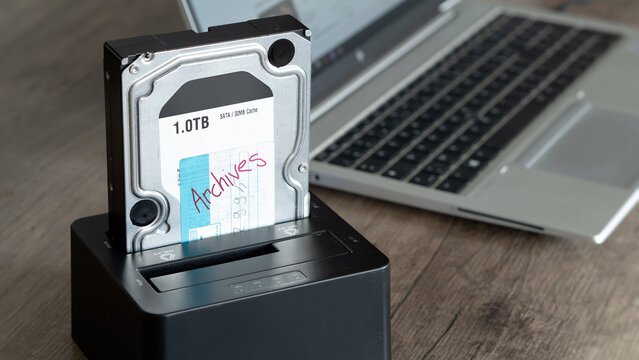 Someone looks at his archives stored on an old hard drive. Docking station with Sata disk drive on a desk.