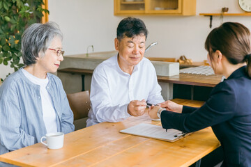 Obraz premium 資産運用・相続税・保険・遺言書の契約書にサインする高齢者夫婦とスーツ姿のアジア人ビジネスウーマン 