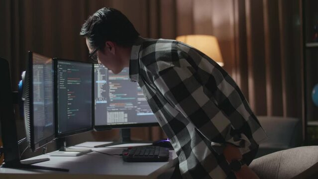 Asian Male Programmer Walking Into The Working Space Before Sitting To Creating Software Engineer Developing App, Program, Video Game On Desktop Computer At Home
