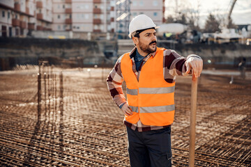 A hardworking site worker is leaning on shovel and looking around site while standing on building foundation. © Dusan Petkovic