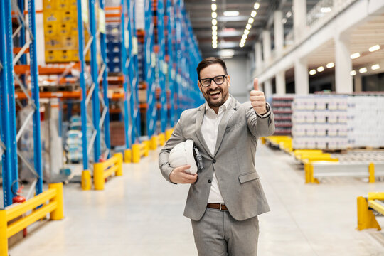 A smiling manager walks in warehouse and giving thumbs up for filled commodity reserves.