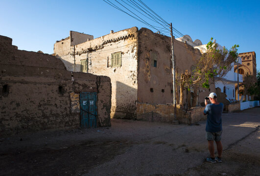 Man tourist photographing old adobe clay houses in village area of Al Bairat, Luxor, Egypt