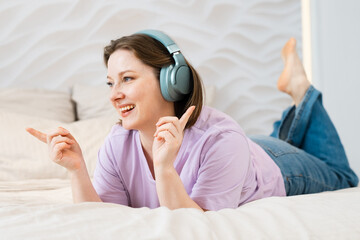Woman lies on the bed in headphones and listens to music.