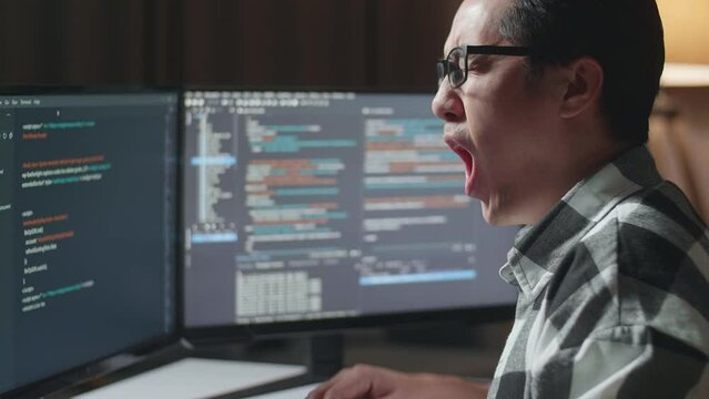 Close Up Of Asian Male Programmer Yawning While Creating Innovative Software Engineer Developing App, Program, Video Game On Desktop Computer At Home. Terminal With Coding Language 

