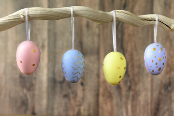 Painted Easter eggs hang on branch against dark wooden background