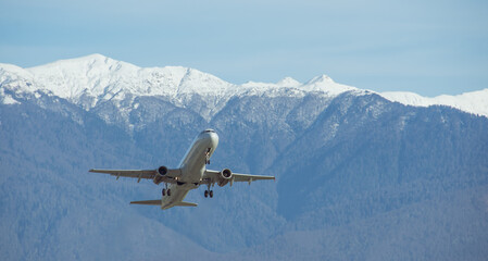 Fototapeta na wymiar Passenger civil aircraft takes off against the backdrop of massive snow capped mountains.