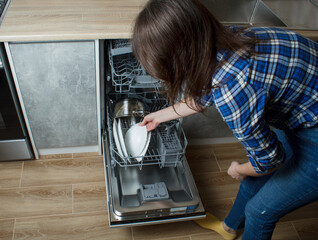 The girl takes out clean dishes from the dishwasher. plate in the hands of a young woman. modern built-in kitchen appliances