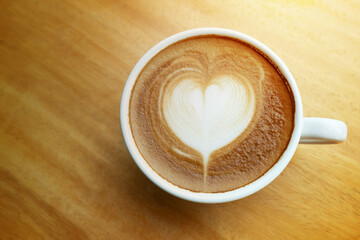 A white cup of latte art coffee heart shape style in the morning time with warm light tone on the wooden desk , top view