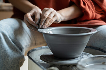 Hands of creative woman sculpture working with potter wheel during production of handmade utensils. Close-up of process of creating clay plate for serving dishes by artisan running small business 