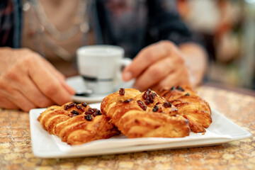 Blurred senior woman sitting at a cafe table while enjoying a break with an espresso coffe cup and a puff pastry