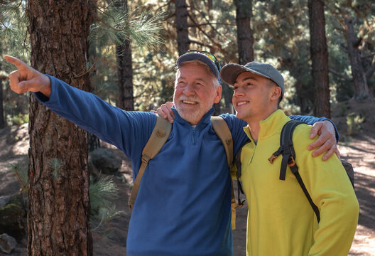 Happy And Carefree Couple Of Grandfather And Teenager Grandson Hiking In The Mountains Sharing Same Passion For Nature And Healthy Lifestyle Together In The Woods. Adventureisageless