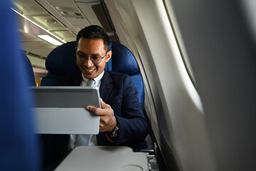 Fototapeta Smiling businessman passenger checking news digital tablet, using wireless connection on board during flight obraz