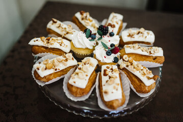 Cupcakes with cream are decorated with raspberries, blueberries and blackberries. Eclairs with cream and nuts.