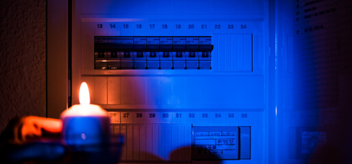 hand holding a candle near an electrical switchboard. Blackout concept