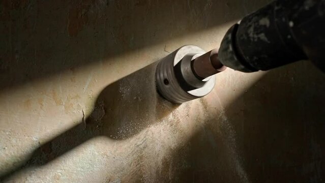 Macro shot of drilling round hole for socket on concrete wall. Metal round nozzle cup rotating on an electric drill or perforator. In process of drilling white dust from the plaster crumbles.