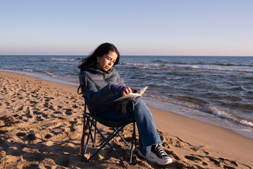 woman reading a book a sunny winter day on the seashore on the beach
