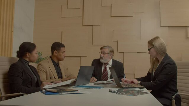 Successful handsome bearded mature male executive and professional diverse multiethnic business team gathering for meeting in boardroom, discussing company finical results and strategy.